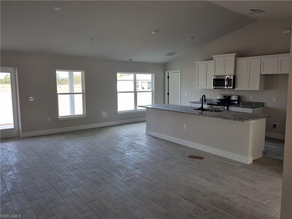 Kitchen with dark stone countertops, an island with sink, stainless steel appliances, white cabinets, and wood tiled floors