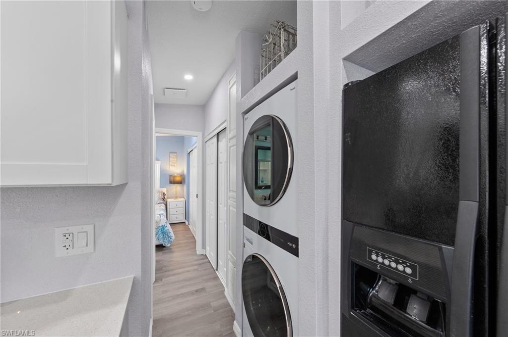 Laundry area with a textured wall, light wood-type flooring, and stacked washer / drying machine