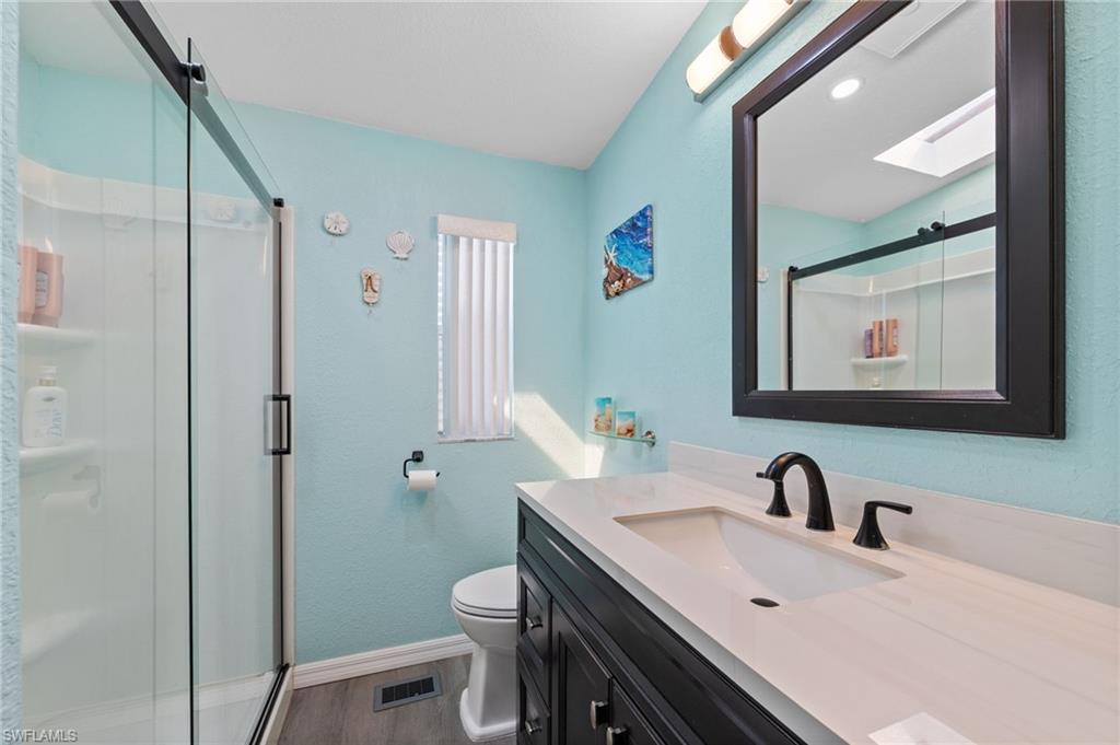 Full bath with vanity, a shower stall, a skylight, and dark wood-type flooring