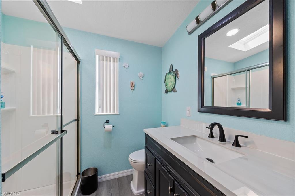 Bathroom with a skylight, a shower stall, vanity, and dark wood finished floors