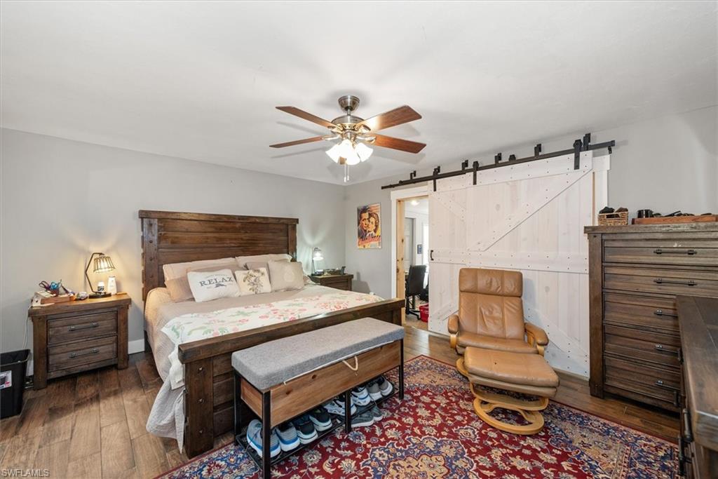 Bedroom featuring a barn door, dark wood-style flooring, and a ceiling fan