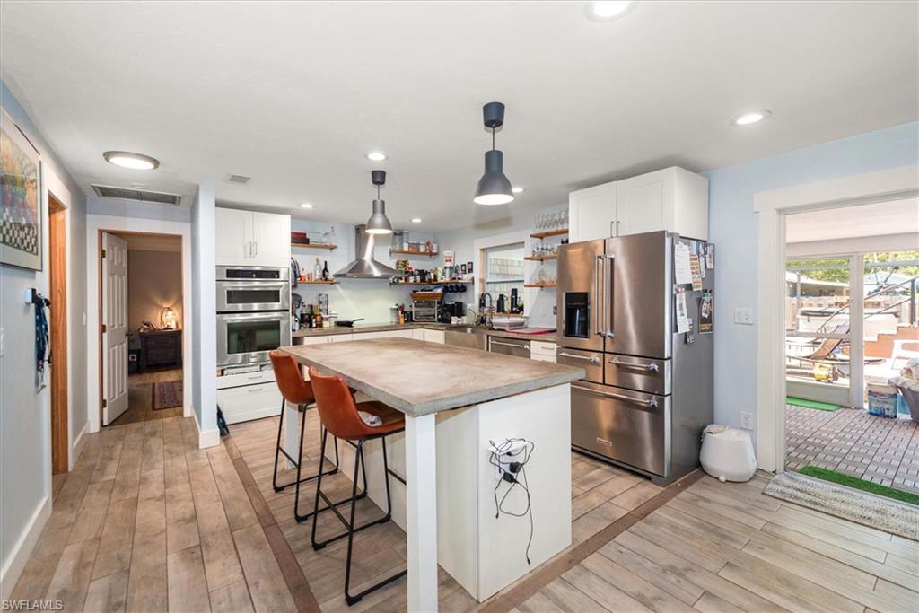 Kitchen featuring white cabinets, stainless steel appliances, a breakfast bar, decorative light fixtures, and light wood finished floors