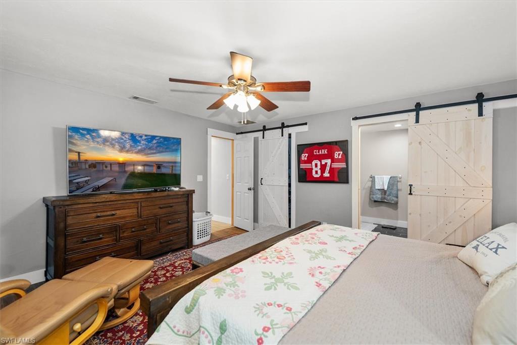 Bedroom with a barn door, ensuite bathroom, and a ceiling fan