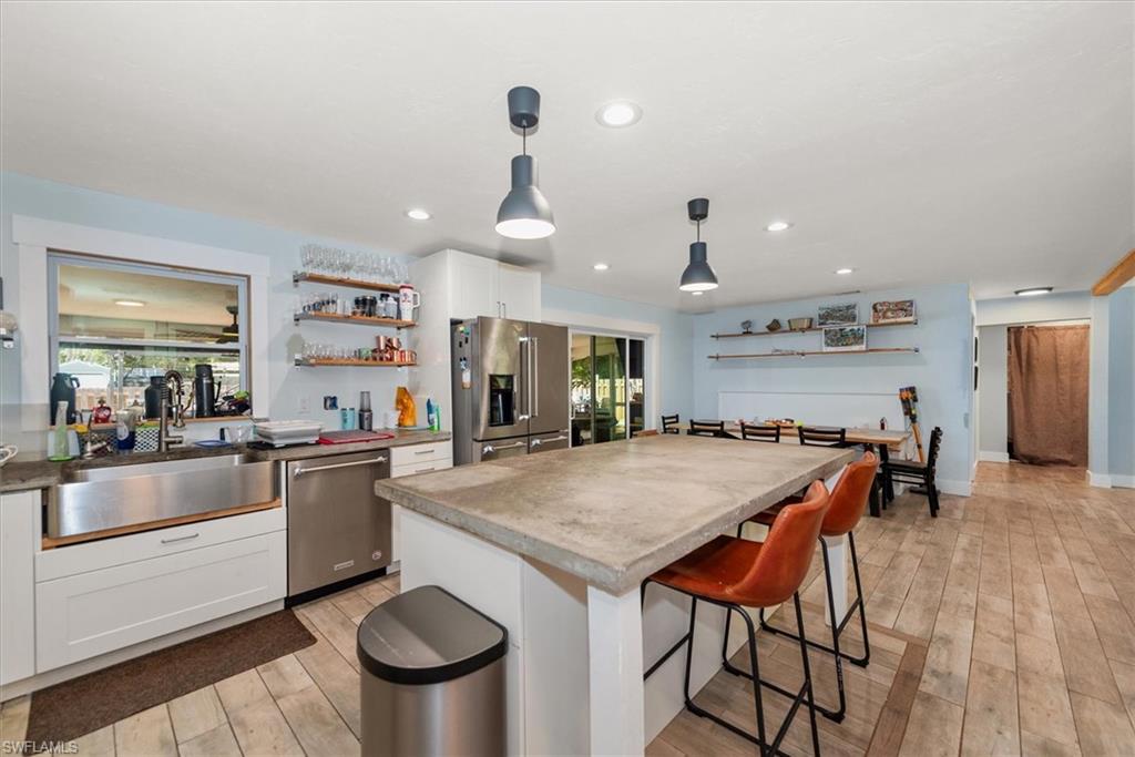 Kitchen featuring white cabinetry, pendant lighting, stainless steel appliances, open shelves, and a breakfast bar area