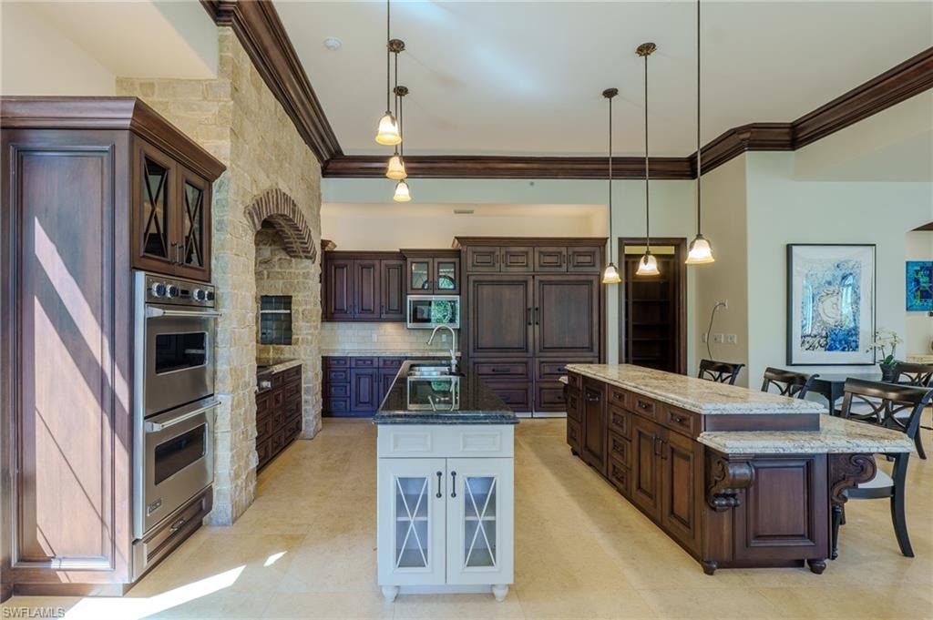 Kitchen with two tone cabinetry, glass insert cabinets, crown molding, a kitchen breakfast bar, and dark stone counters