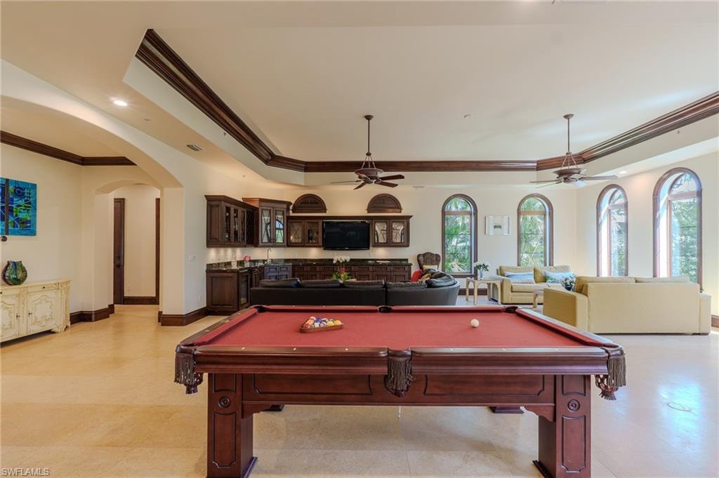Playroom with ornamental molding, pool table, a tray ceiling, arched walkways, and ceiling fan