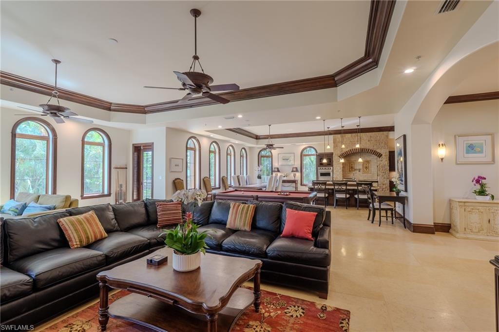 Living area with ornamental molding, a tray ceiling, a ceiling fan, arched walkways, and plenty of natural light