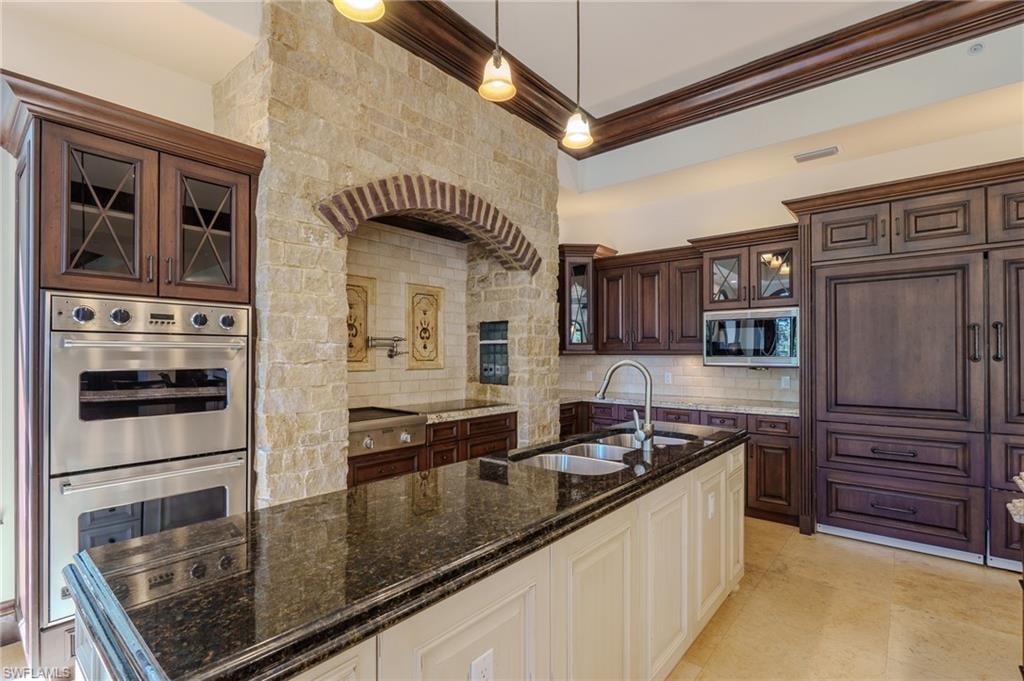 Kitchen featuring glass insert cabinets, two tone color scheme, stainless steel appliances, dark stone counters, and backsplash