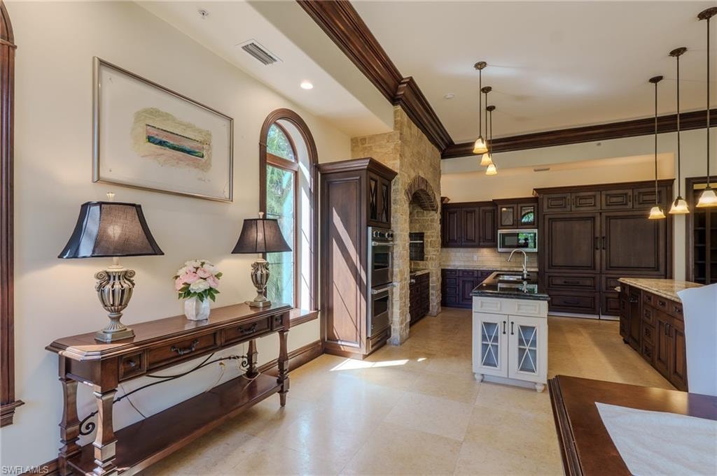 Two tone kitchen featuring dual tone cabinetry, crown molding, dark stone countertops, tasteful backsplash, and hanging light fixtures