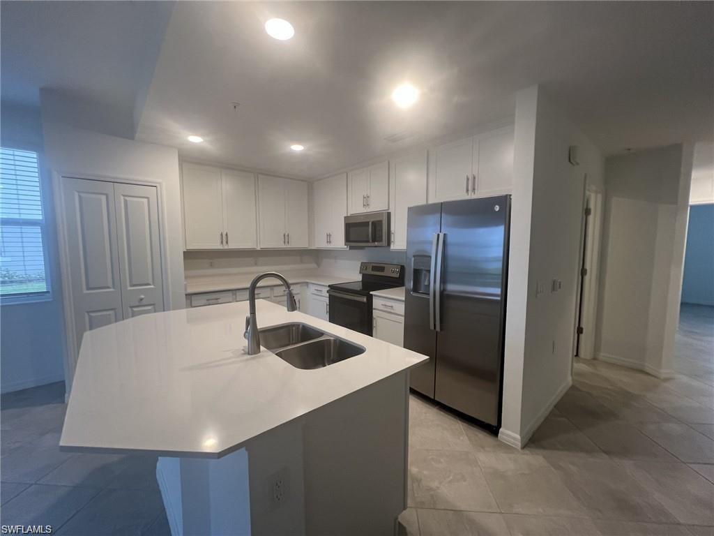 Kitchen with stainless steel appliances, white cabinets, an island with sink, recessed lighting, and light stone countertops