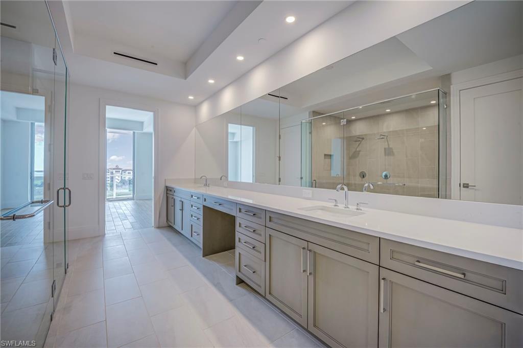 Bathroom featuring double vanity, a raised ceiling, a shower stall, recessed lighting, and light tile patterned floors