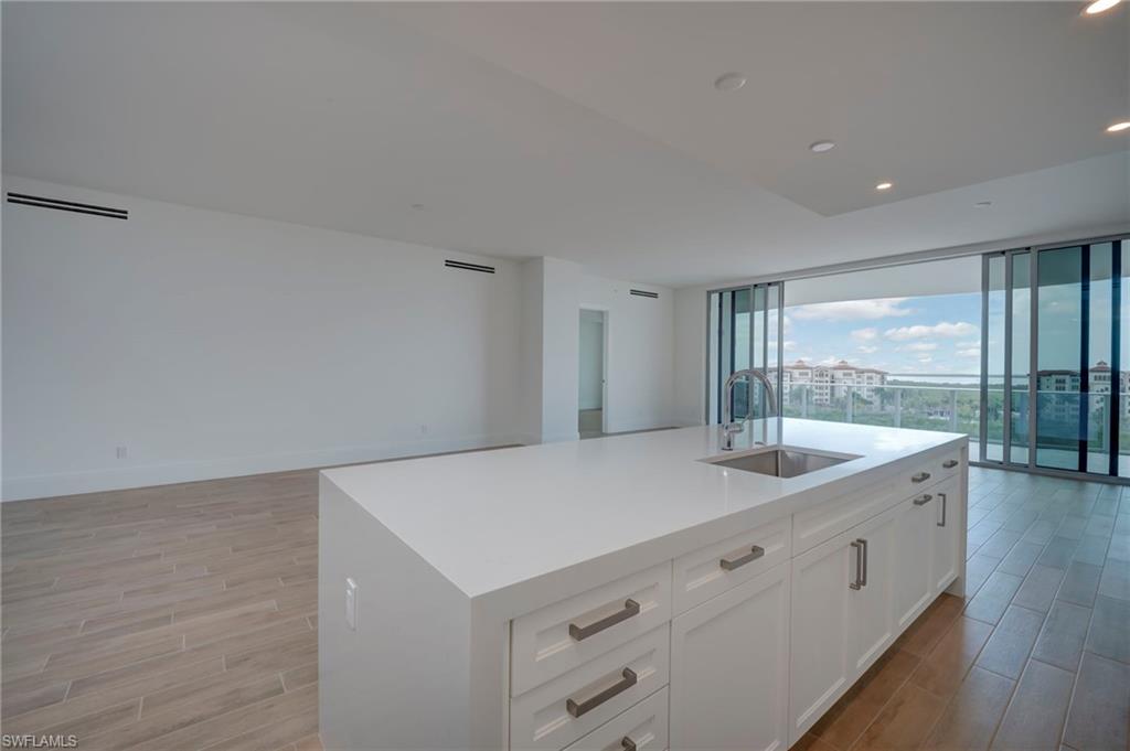 Kitchen featuring expansive windows, wood tiled floors, white cabinetry, an island with sink, and light stone countertops