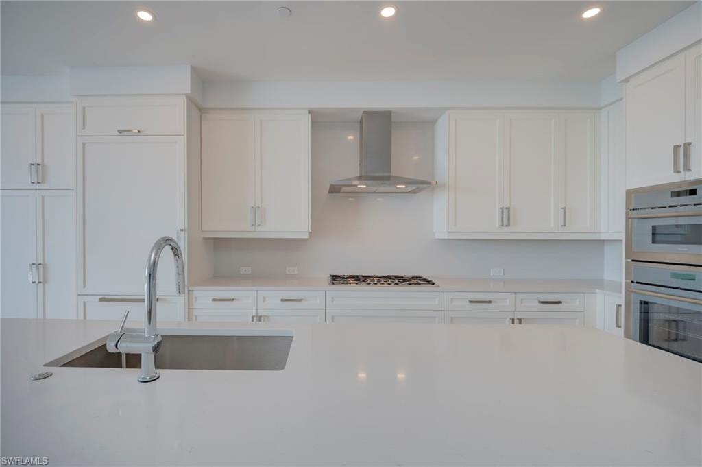 Kitchen with recessed lighting, range hood, white cabinets, stainless steel appliances, and light stone counters