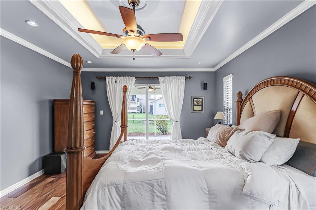 Bedroom with access to outside, ornamental molding, wood finished floors, ceiling fan, and a raised ceiling