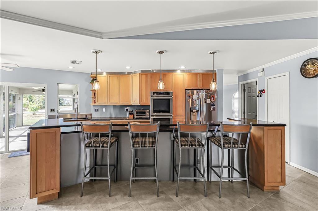 Kitchen with stainless steel appliances, crown molding, decorative light fixtures, wood finish cabinets, and a kitchen breakfast bar