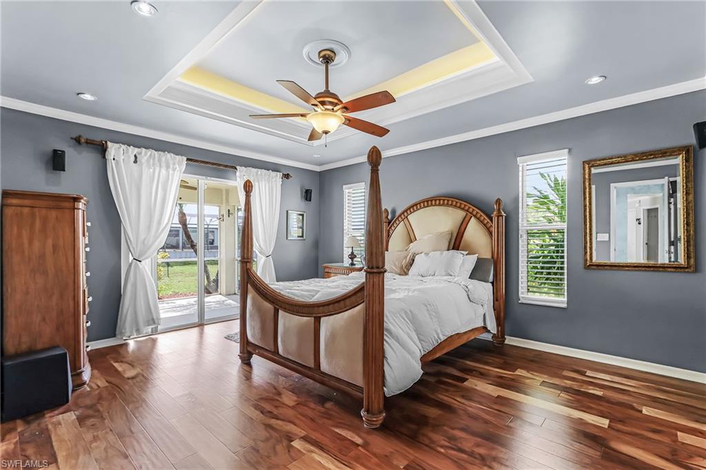 Bedroom featuring dark wood-style floors, access to outside, a ceiling fan, ornamental molding, and multiple windows