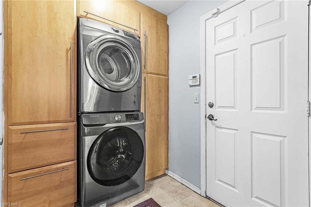 Laundry room with cabinet space, stacked washing machine and dryer, and light tile patterned floors