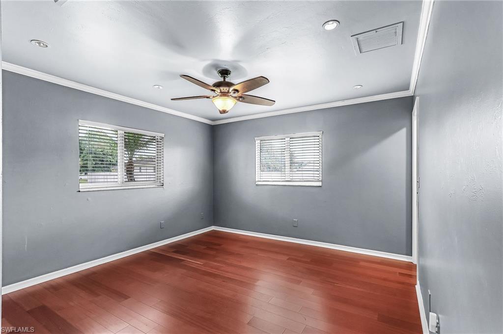 Empty room with ceiling fan, dark wood-type flooring, crown molding, and healthy amount of natural light