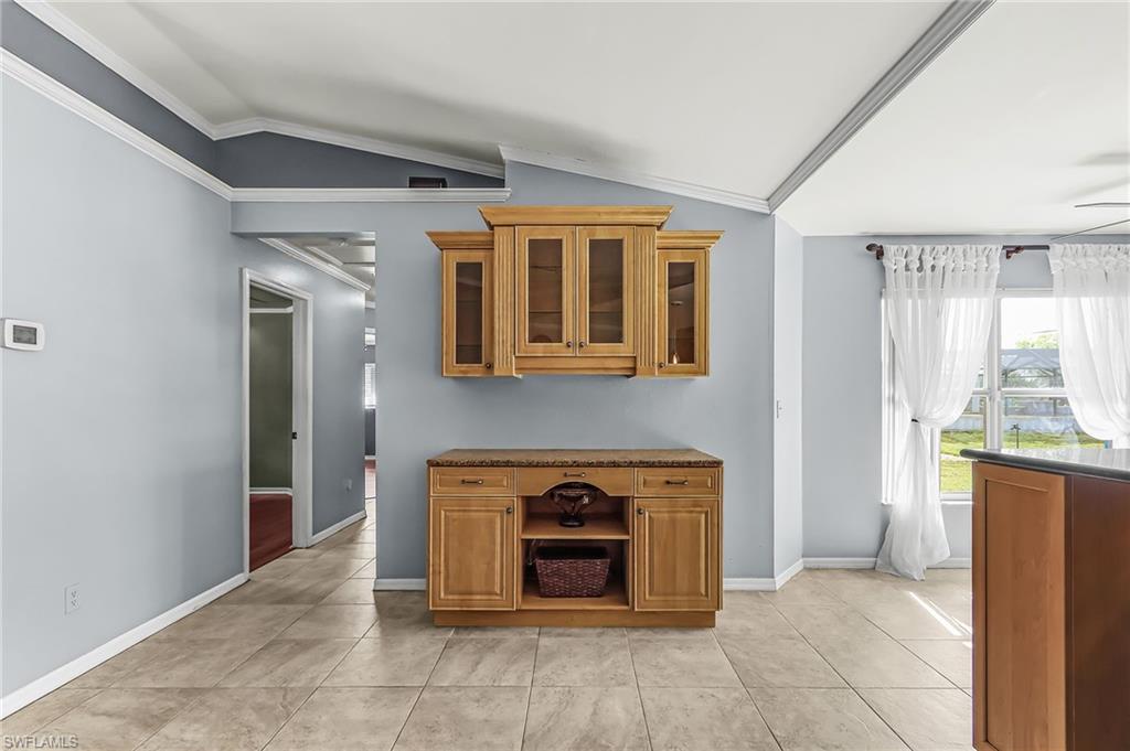 Kitchen featuring ornamental molding, lofted ceiling, wood finish cabinets, glass fronted cabinets, and light tile patterned flooring