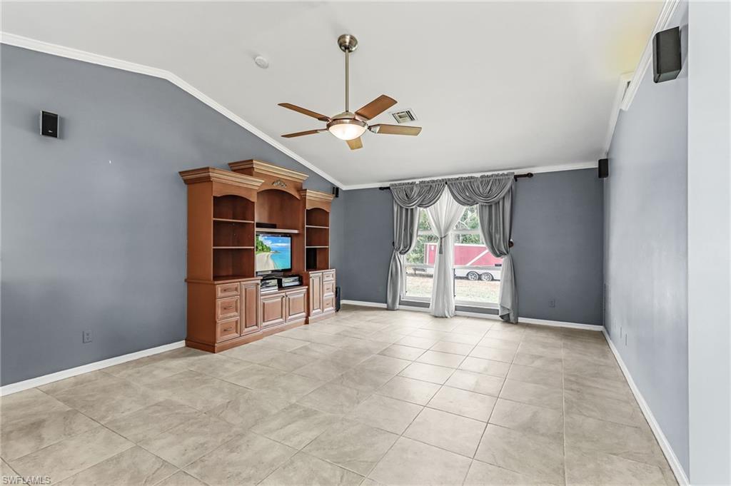 Unfurnished living room with ceiling fan, ornamental molding, vaulted ceiling, and light tile patterned floors