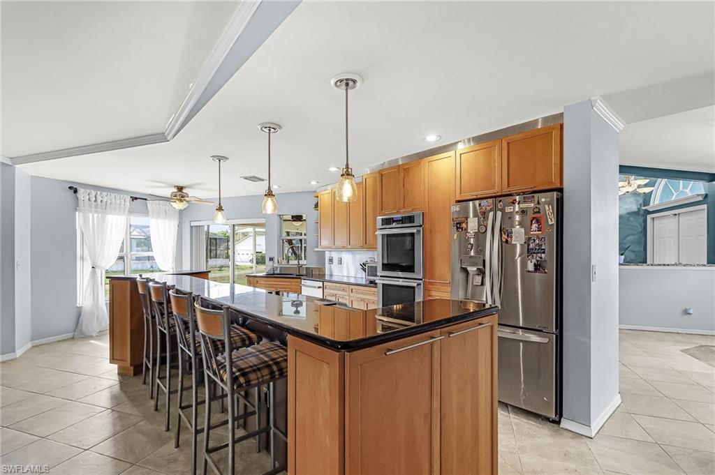 Kitchen featuring stainless steel appliances, wood finish cabinets, light tile patterned floors, decorative light fixtures, and a spacious island