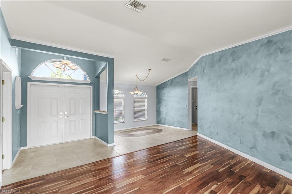 Foyer with ornamental molding, wood finished floors, vaulted ceiling, and hanging lights