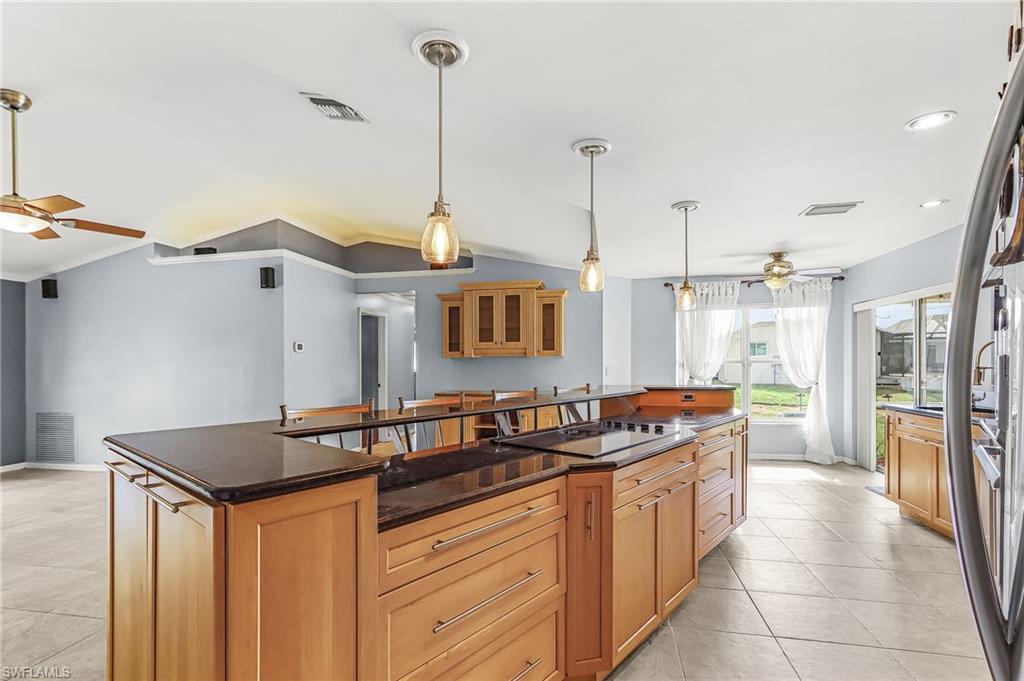 Kitchen with ceiling fan, a kitchen island with sink, dark stone counters, decorative light fixtures, and crown molding