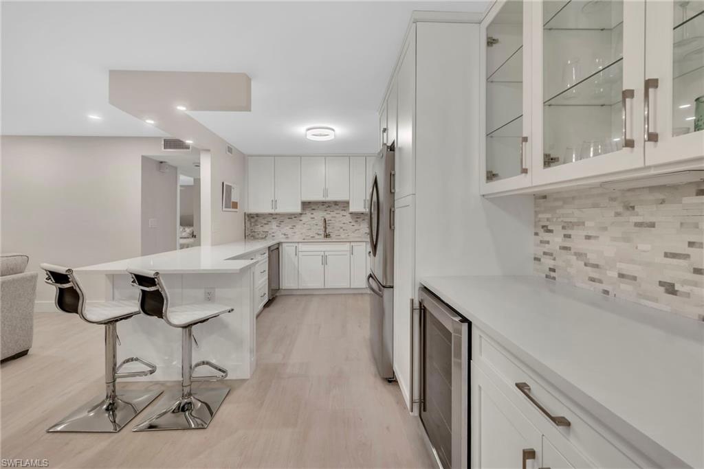 Kitchen with a peninsula, white cabinetry, wine cooler, a breakfast bar, and glass fronted cabinets