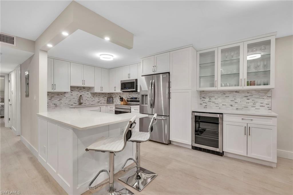Kitchen featuring wine cooler, stainless steel appliances, white cabinets, glass fronted cabinets, and a peninsula