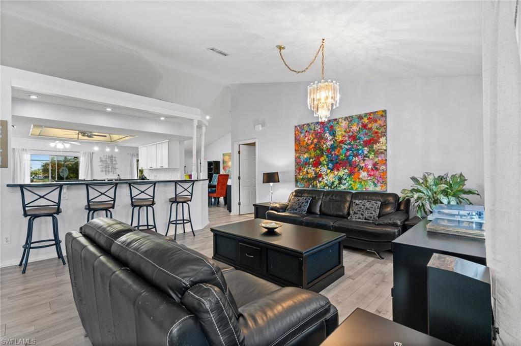 Living room featuring suspended lighting, light wood-style flooring, and vaulted ceiling