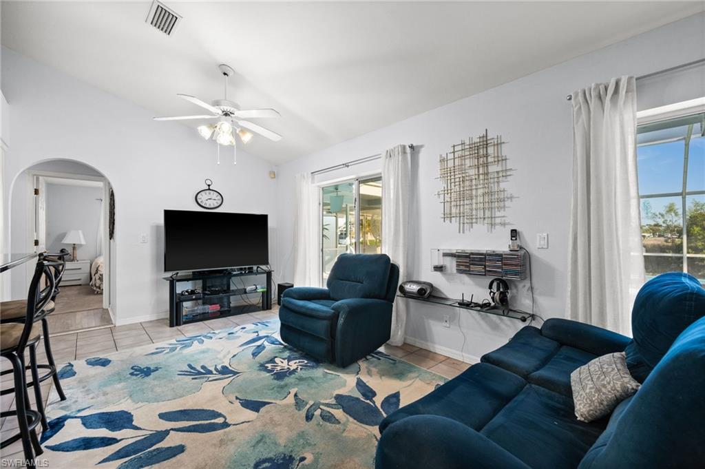 Living area with vaulted ceiling, light tile patterned floors, arched walkways, and ceiling fan