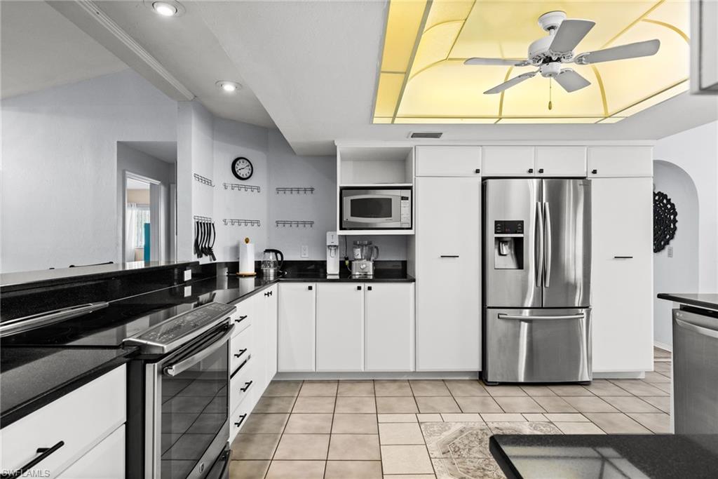 Kitchen featuring stainless steel appliances, white cabinets, a ceiling fan, dark stone countertops, and light tile patterned flooring