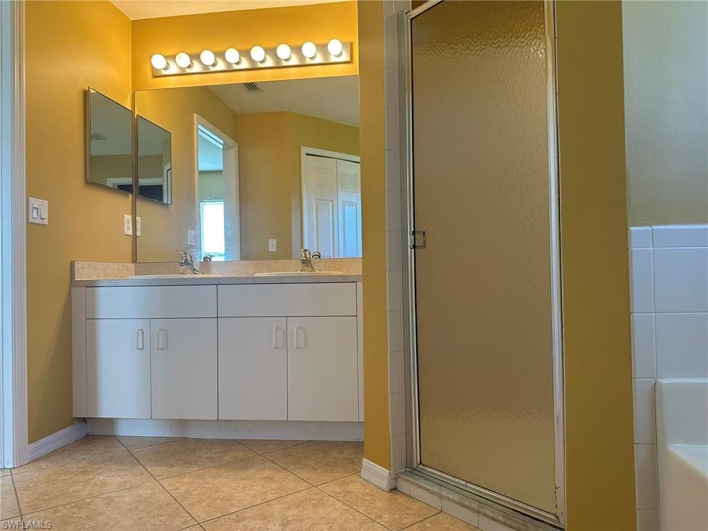 Full bathroom featuring double vanity, a shower stall, light tile patterned flooring, and a garden tub