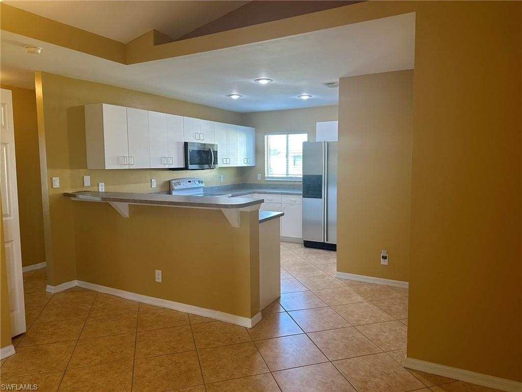 Kitchen with a peninsula, a breakfast bar area, white cabinets, stainless steel appliances, and light tile patterned flooring