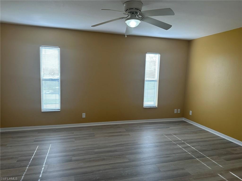 Empty room with dark wood-style flooring, ceiling fan, and plenty of natural light
