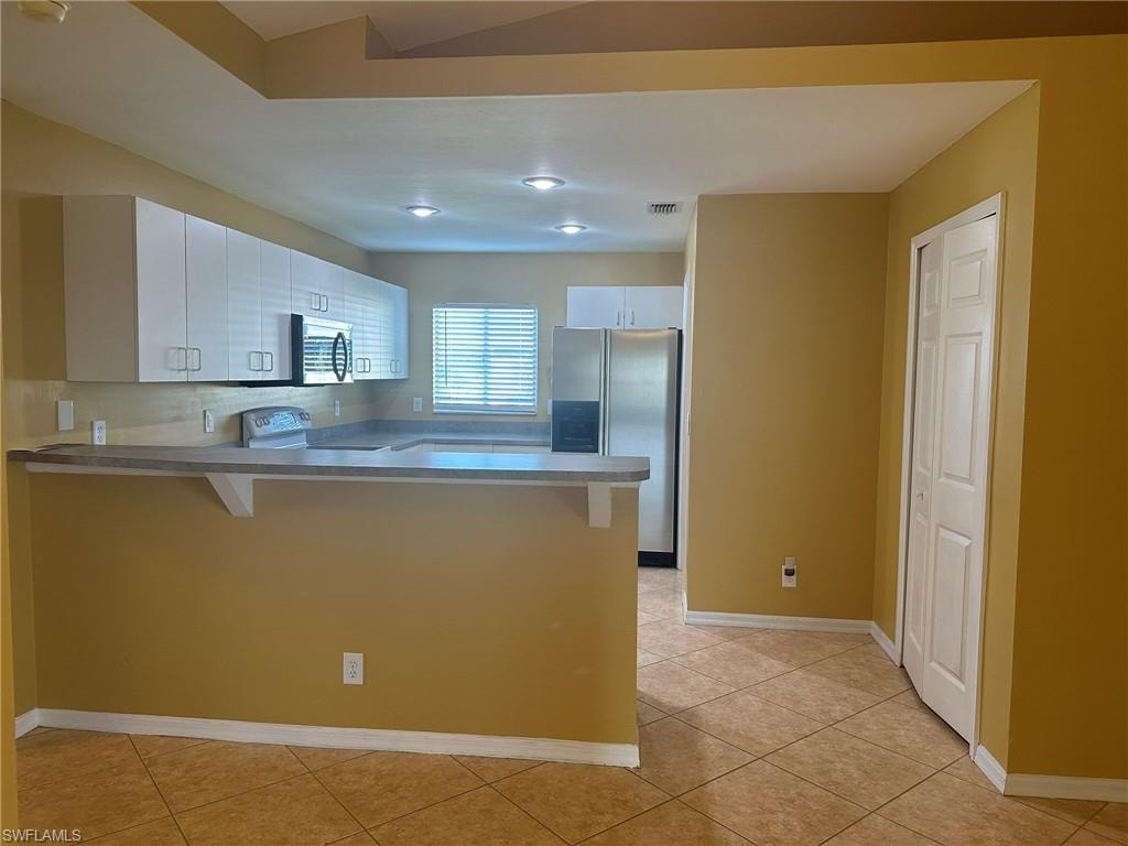 Kitchen featuring a kitchen breakfast bar, a peninsula, stainless steel appliances, and dark countertops