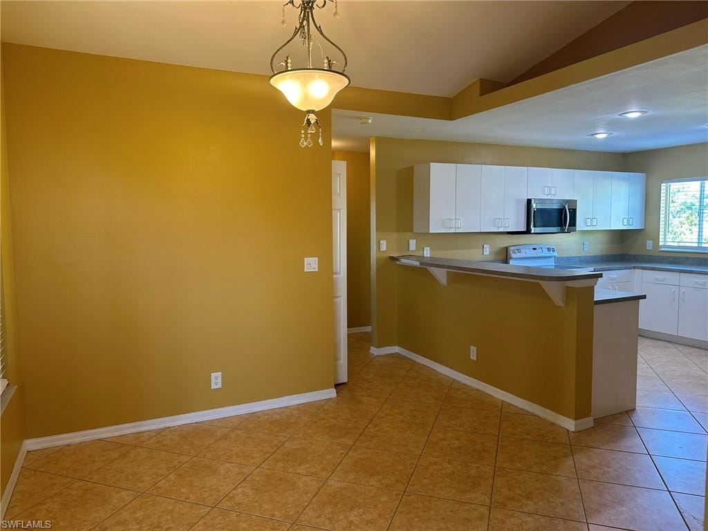 Kitchen with a peninsula, white cabinetry, a kitchen breakfast bar, pendant lighting, and stainless steel microwave