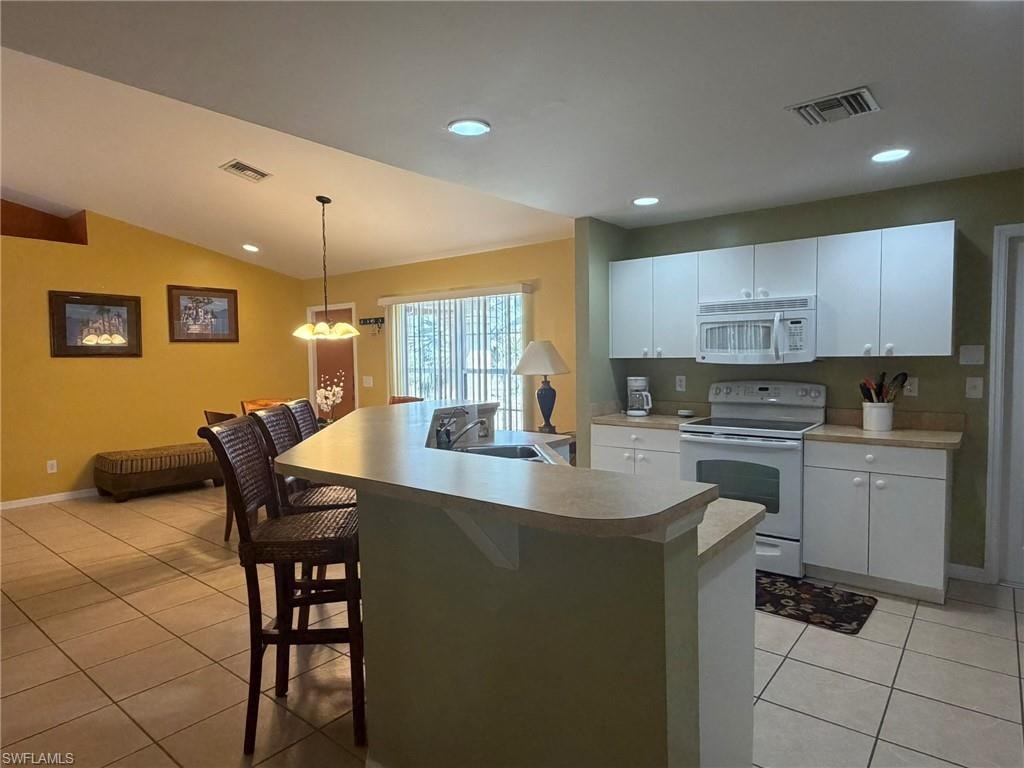 Kitchen featuring white appliances, a kitchen bar, white cabinets, an island with sink, and light tile patterned floors