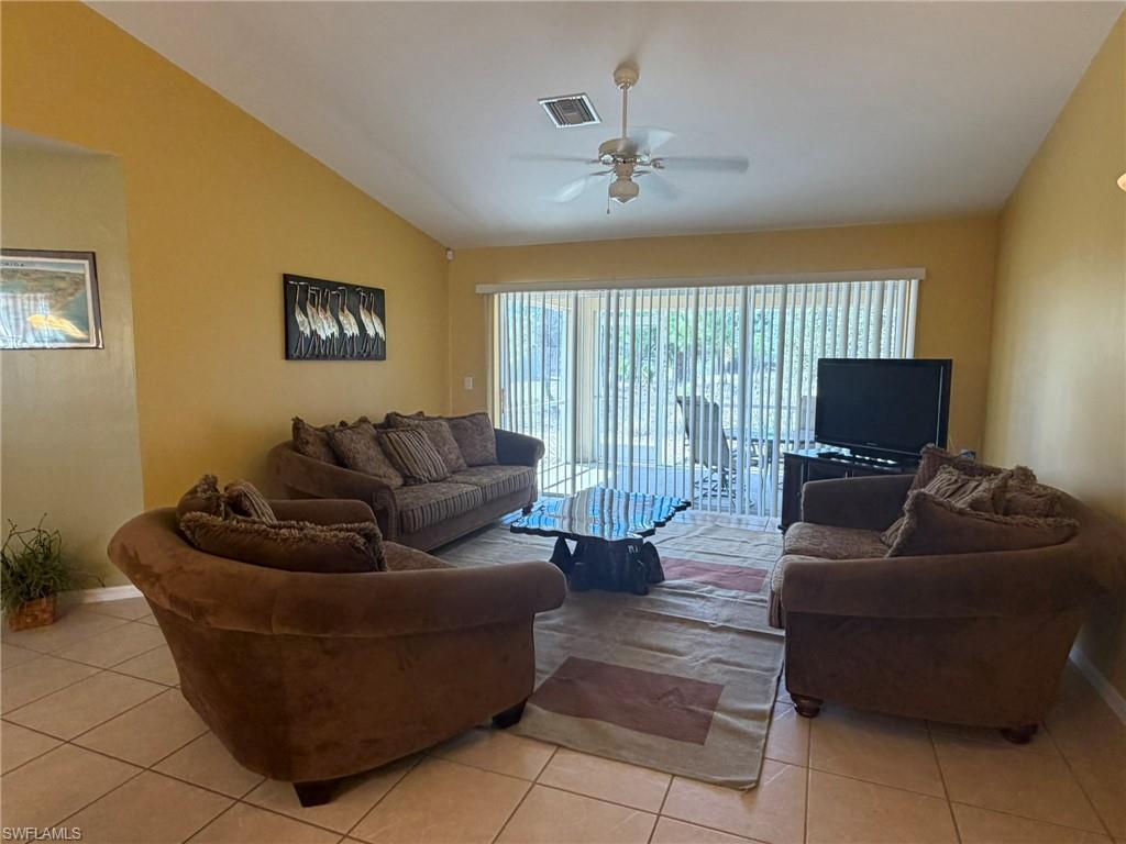 Living room with a ceiling fan, lofted ceiling, and light tile patterned flooring