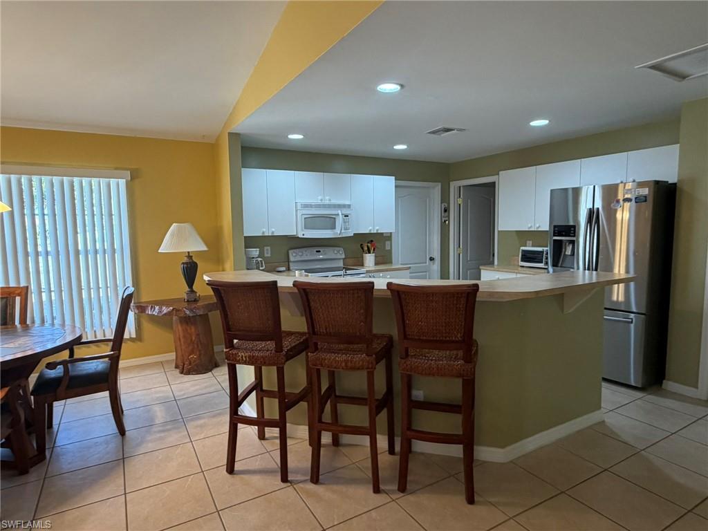 Kitchen with a breakfast bar, light countertops, white appliances, white cabinets, and light tile patterned flooring