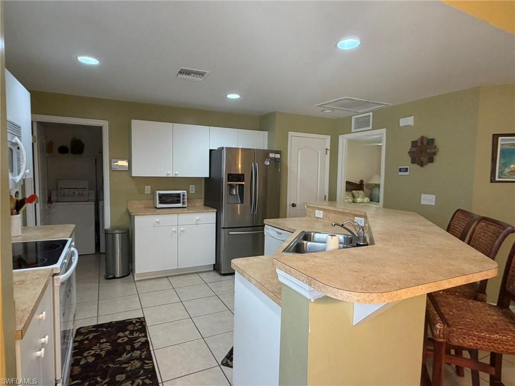 Kitchen featuring a breakfast bar area, white appliances, a large island with sink, light countertops, and recessed lighting