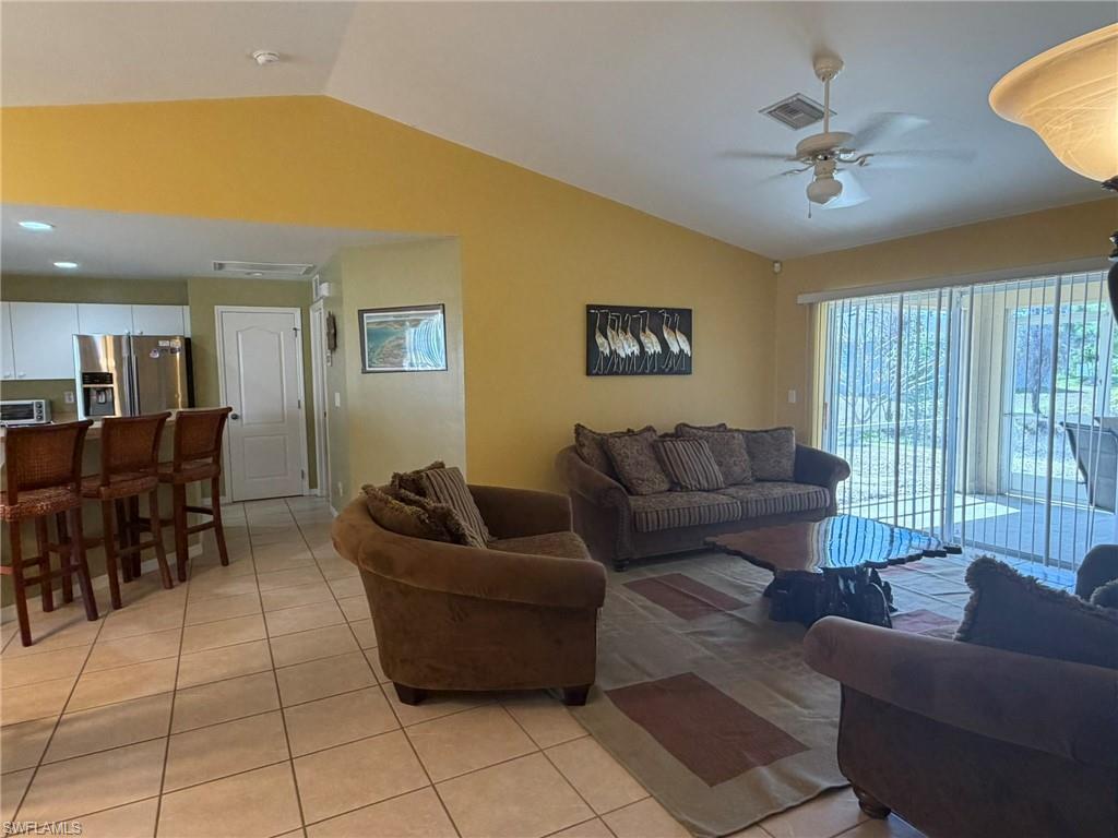 Living room with light tile patterned floors, vaulted ceiling, and a ceiling fan