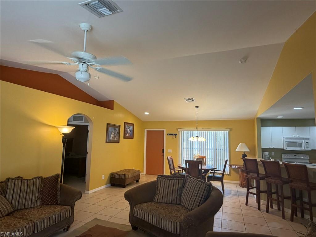 Living room with light tile patterned floors, lofted ceiling, ceiling fan, recessed lighting, and arched walkways