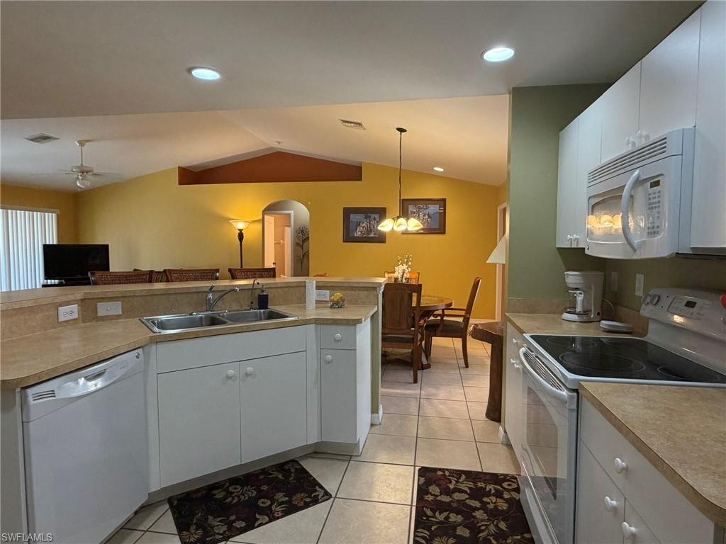 Kitchen with white appliances, arched walkways, vaulted ceiling, decorative light fixtures, and light tile patterned floors