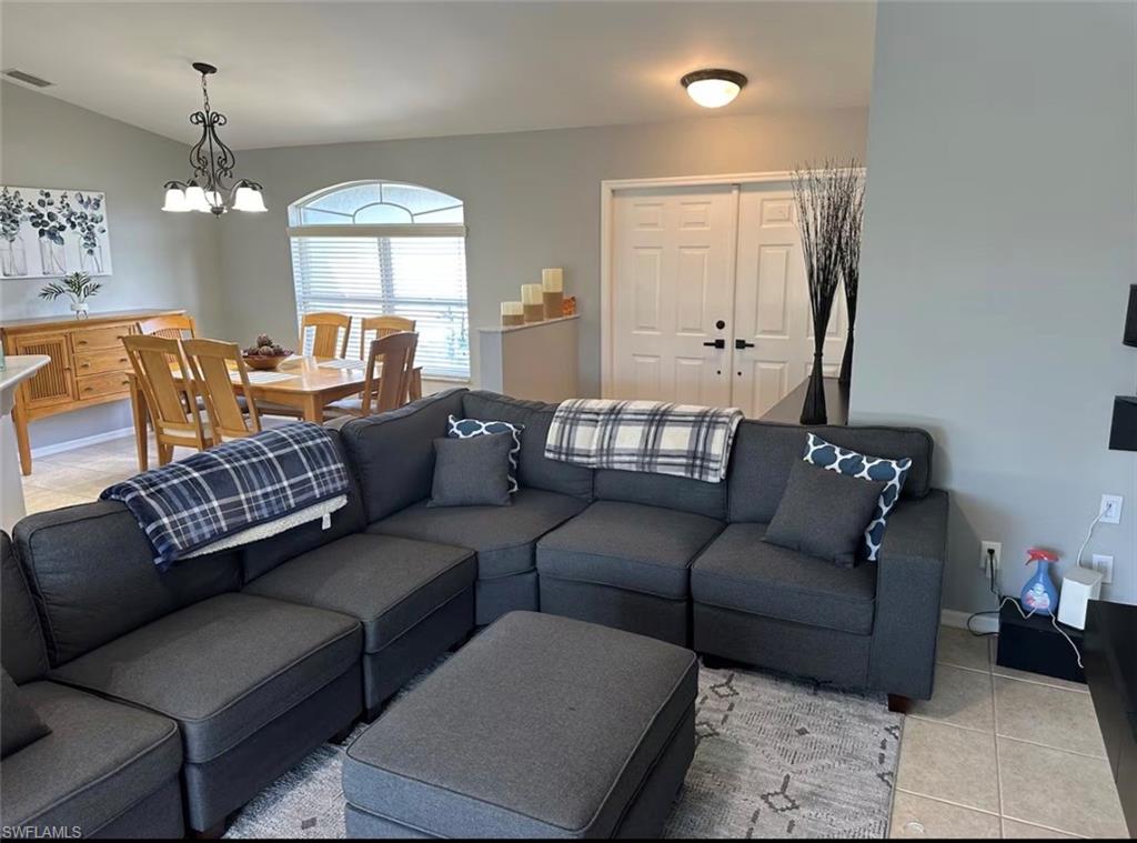 Living room featuring suspended lighting, light tile patterned flooring, and vaulted ceiling