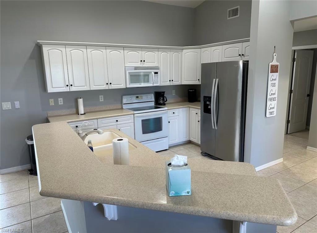 Kitchen with light tile patterned flooring, white cabinets, white appliances, and a breakfast bar