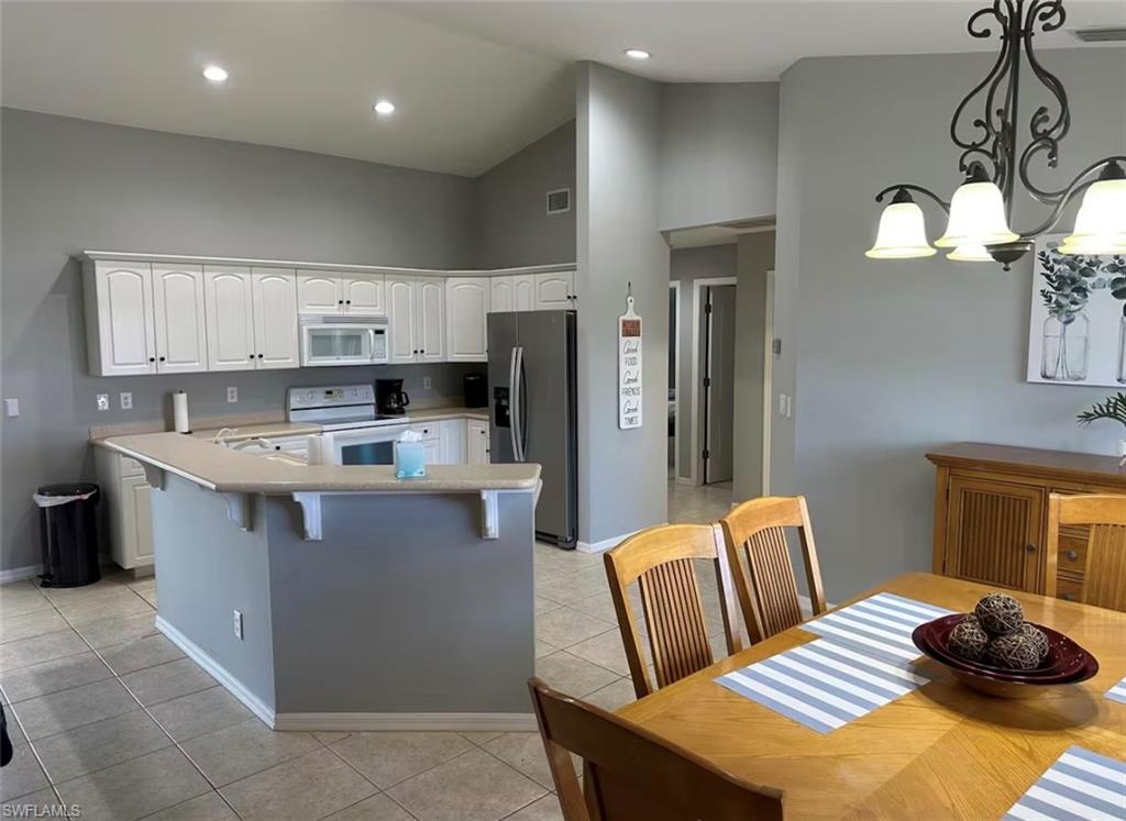 Kitchen featuring lofted ceiling, white cabinets, white appliances, light countertops, and a kitchen bar