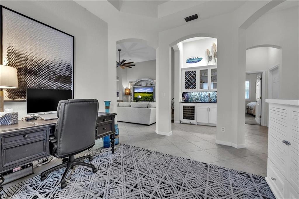 Office space with beverage cooler, a dry bar, a high ceiling, light tile patterned flooring, and a ceiling fan