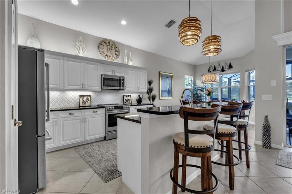 Kitchen featuring an island with sink, a breakfast bar area, stainless steel appliances, light tile patterned floors, and white cabinetry