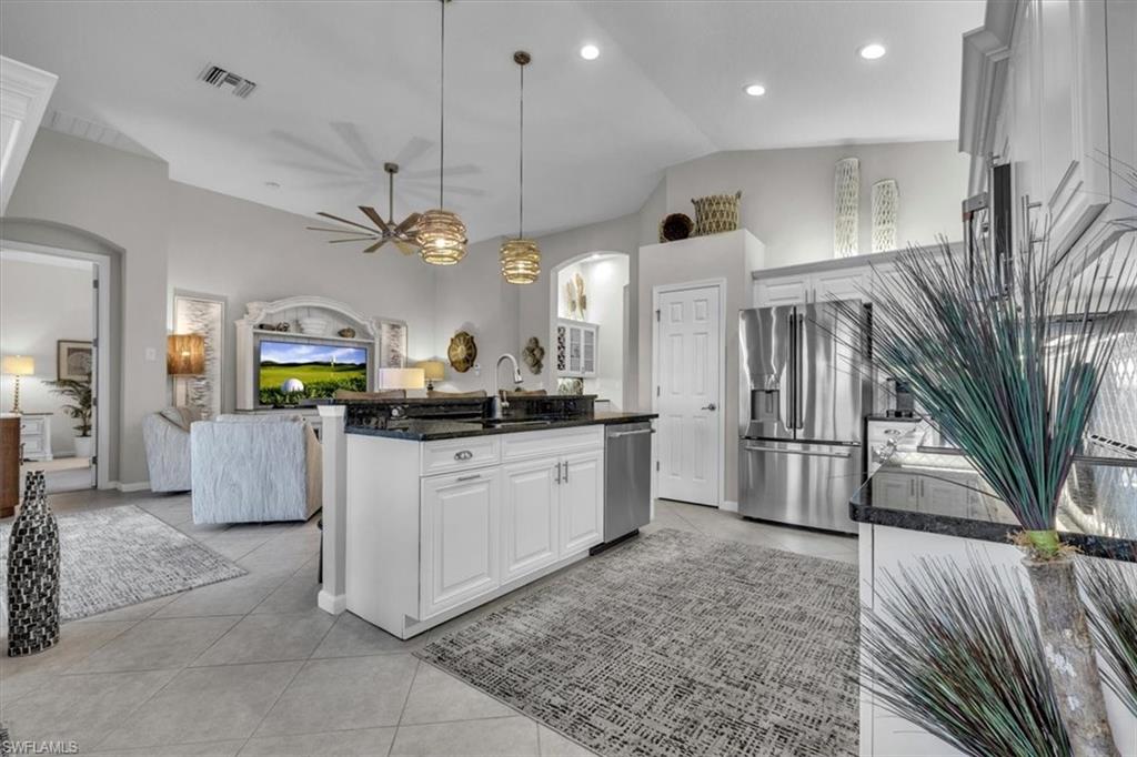 Kitchen featuring dark stone counters, stainless steel appliances, arched walkways, white cabinets, and lofted ceiling